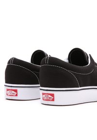 Fekete vászon slip-on cipők fehér varrással és texturált felsőrésszel. Fehér gumi talp, a sarkán piros "VANS OFF THE WALL" logóval.