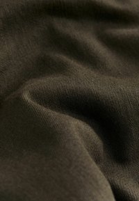 Tumepruun kangas, mille pind on sile ja veidi tekstuuriga, näitab õrnade voldikute ja langevuste märke. Materjal näib pehme ja paindlik.