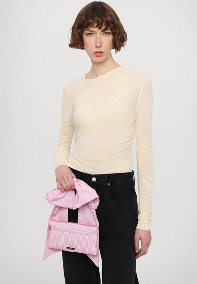 Cream, long-sleeve top with twisted texture; model holding a pink bag with a wavy pattern and flap; black jeans; minimalistic design.