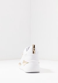 Weiße Sneaker mit goldenen Akzenten, glattem Kunstledermaterial, gepolstertem Schaft und kantigen Designelementen an der Ferse und den Seiten.