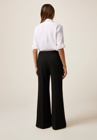 Camicia bianca con colletto e maniche arrotolate, abbinata a pantaloni neri a vita alta e gamba larga. Tessuto morbido con una vestibilità comoda e una vita elastica.