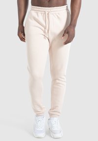 Helle beige Sweatpants mit elastischem Bund, Kordelzug, schmalem Schnitt und gerippten Bündchen. Dazu weiße Sneaker.
