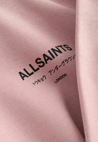 Svijetlo ružičasta tkanina glatke teksture, sa crnim natpisima "ALLSAINTS" i "LONDON", uz dodatne japanske karaktere.