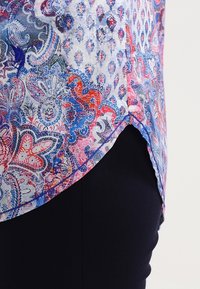 Multicolored blouse with paisley and floral patterns in blue, red, and white; rounded hem; lightweight fabric; side split detail.