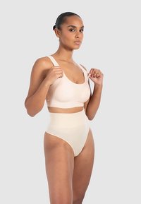 Beżowy sportowy biustonosz z szerokimi ramiączkami, zestawiony z wysokim stanem, bezszwową bielizną w kolorze nude. Gładka tkanina i dopasowany krój zapewniają odpowiednie krycie.