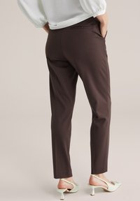 Hnedé slim-fit nohavice s hladkou textúrou, obsahujúce zadné vrecko. V páre s mätovozelenými topánkami na nízkom podpätku s otvoreným dizajnom.