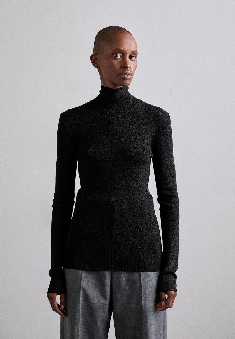 Mustra mustriga mustre pikkade varrukatega must turtleneck-sviiter. Valmistatud tekstuurist, sädelevast kangast. Kombineeritud hallide kohandatud pükstega.