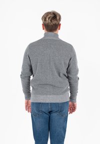 Grijze gebreide trui met hoge kraag, ribgebreide manchetten en zoom, gecombineerd met blauwe spijkerbroek. Het ontwerp heeft een gladde textuur en een getailleerde pasvorm.