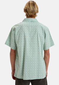 Camicia a maniche corte in verde menta chiaro, con un delicato motivo floreale e colletto standard, realizzata in tessuto morbido con vestibilità comoda.
