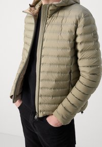 Helle olivgrüne Pufferjacke mit horizontalen Nähten, einem Reißverschluss auf der Vorderseite und Kapuze. Verfügt über elastische Bündchen und seitliche Taschen zur Aufbewahrung.