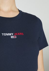 Marinblå bomullst-shirt med rund halsringning. Har broderad "TOMMY JEANS" i vitt och rött på vänster bröstområde. Korta ärmar.