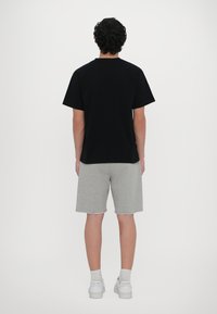 Svart kortermet t-skjorte med rund hals, kombinert med grå shorts og hvite joggesko. Enkelt design, avslappet passform og bomullsstoff.