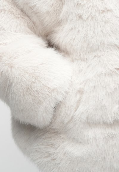 Világos színű műszőrmeanyag, puha, bolyhos textúrával és finom fényességgel. Közeli kép, amely kiemeli a sűrű, megnyúlt szálakat.