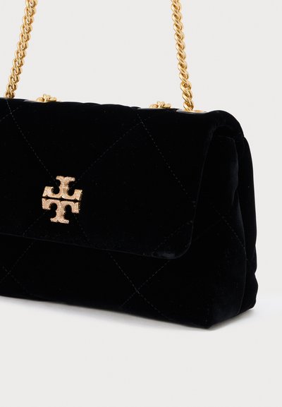 Mala de veludo preta com padrão matelassê, com alça de corrente dourada e detalhe de logotipo dourado na parte frontal.