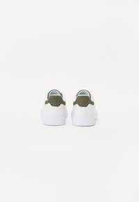 Hvite sneakers med en glatt finish, med oliven grønn semsket skinn detaljer på hælene og en strukturert hvit gummisåle.