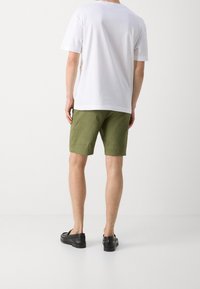 Biała bawełniana koszulka, krótki rękaw, w połączeniu z oliwkowo-zielonymi szortami. Czarne buty typu slip-on z teksturowanymi detalami. Minimalistyczny design, neutralne kolory.