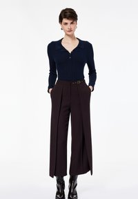 Marineblaues, gerippte Langarmoberteil mit Kragen und Knopfleiste, kombiniert mit hoch taillierten, dunkelbraunen, plissierten Hosen mit Gürtel.
