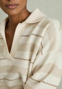 Cremefarvet strikket oversized sweater med V-udskæring og lysebrune striber. Har en blød tekstur og et kravedesign ved halsudskæringen.