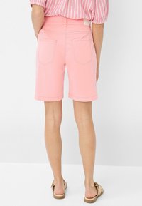 Lichtroze denim shorts met een rechte snit, omgeslagen zomen en twee achterzakken. G gedragen met beige sandalen, gezien van achteren.