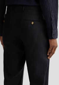 Dunkelblaues Hosen aus strukturiertem Stoff, mit schlanker Passform, zwei Gesäßtaschen mit goldenen Knopfakzenten und einem glatten Bund.