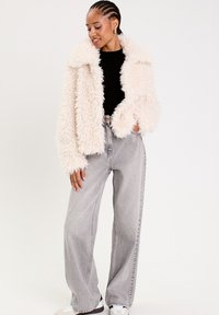 Veste en fourrure crème avec un large col, portée sur un haut noir, associée à un jean gris taille haute et des baskets blanches.