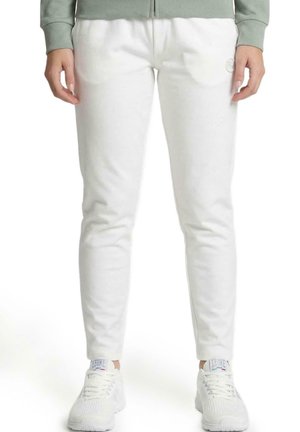 Un mannequin cadré partiellement porte un pantalon de jogging blanc fuselé, avec un petit logo sur la cuisse, des baskets blanches et un sweat-shirt vert sauge.