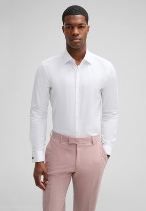 White button-up shirt with a structured collar, complemented by light pink textured trousers and contrasting black cuff accents.