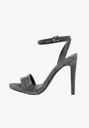 Sandale noire à talons hauts avec lanière de cheville et boucle, recouverte de petits rhinestones scintillants, design à bout ouvert sur fond blanc.