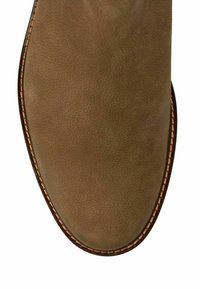 Parte superiore della scarpa in suede marrone con una texture liscia, caratterizzata da una punta arrotondata e cuciture a contrasto lungo la suola.