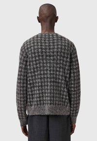 Grå og svart rutet strikkegenser med myk tekstur, rund halslinje og litt løs passform, vist fra baksiden.