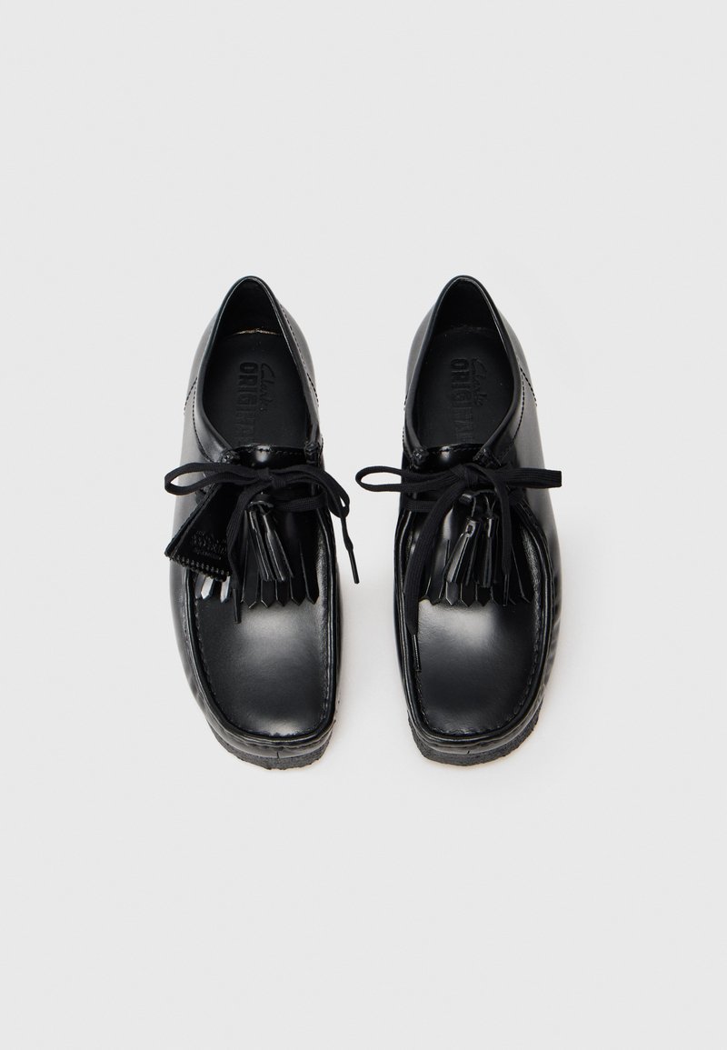 Black leather shoes with a glossy finish, rounded toe, and a lace-up design. Features a decorative tassel accent and textured sole.