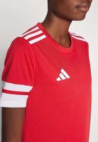 Rood sportshirt met witte mouwaccenten en drie witte strepen op de schouders. Bevat een wit Adidas-logo op de borst.