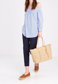 Blusa a righe blu e bianca con spalle scoperte, pantaloni a righe blu navy, scarpe espadrillas marroni e una grande borsa in rafia intrecciata.