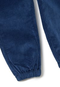 Blaue Cord-Hosen mit elastischen Bündchen, aus dem Bereich des Unterschenkels gegen einen weißen Hintergrund gezeigt.