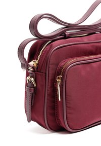 Bordowa torebka na ramię z gładkiego nylonu, wyposażona w złote okucia zamka błyskawicznego, podwójne przegrody na zamek oraz płaską regulowaną rączkę.