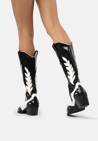 Botas de cowboy en blanco y negro con un patrón de hojas, diseño estructurado, tacón bloque de altura media y cremalleras a los lados.