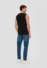 Black sleeveless shirt with a round neck, paired with light blue denim jeans. Model is wearing white sneakers, viewed from the back.