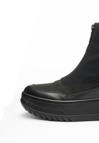 Botas negras hasta el tobillo con una combinación de cuero liso y tejido texturizado. Suela de plataforma gruesa con un patrón geométrico. Cierre de cremallera en el lateral.