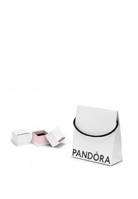 Sac cadeau blanc avec une poignée noire étiqueté "PANDORA," à côté de deux boîtes à bijoux : une blanche et une rose avec un intérieur noir.