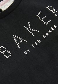 Camiseta de algodón negra con "BAKER" en strass plateados, con "by TED BAKER" en un texto más pequeño debajo. Vista en primer plano de la tela y el diseño.