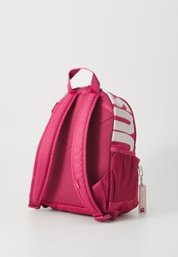 Rosa tygryggsäck med vadderade axelremmar, sidofack i nät och en vit logotyp. Har en liten etikett med texten "Just Do It".