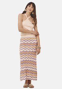 Top sin mangas de color beige claro con tirantes entrecruzados, combinado con una falda larga de patrón zigzagueante en naranja pastel, lavanda y blanco.
