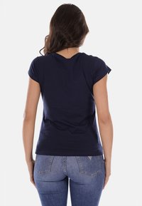 T-shirt a maniche corte blu navy realizzato in cotone, con un design semplice, scollatura rotonda e vestibilità slim. Vista posteriore mostrata con jeans.