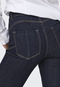 Donker denim jeans met twee achterzakken, contrasterende stiksels en een middelhoge taille. Glad textuur en aansluitend ontwerp.