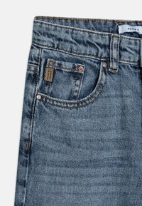 Jean en denim de couleur bleu délavé avec un design classique. Comprend une poche avant, des coutures contrastantes et une petite étiquette de marque près de la taille.
