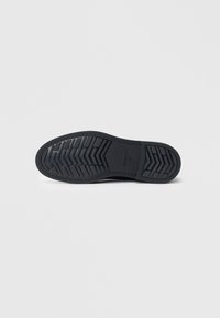Semelle de chaussure noire avec un motif de crantage en chevron et marquage de taille 41 sur un fond blanc uni.