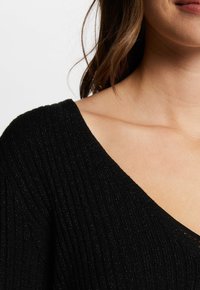 Maglione nero a V con texture a costine. Caratterizzato da una leggera lucentezza e una silhouette aderente, mette in risalto un collo e un'area spalle morbidi.