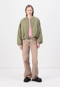 Olijfgroene bomberjack, roze shirt, beige high-waisted jeans en zwarte platform schoenen. Zachte stof, relaxte pasvorm en oversized ontwerp.