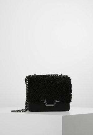 Czarna teksturowana torebka z srebrnym łańcuszkiem i geometrycznym srebrnym zapięciem, prezentowana na białym postumencie na szarym tle.