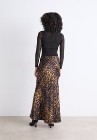 Top negro de manga larga combinado con una falda maxi de estampado de leopardo en tonos de amarillo y marrón; tejido suave; llevado con tacones negros.